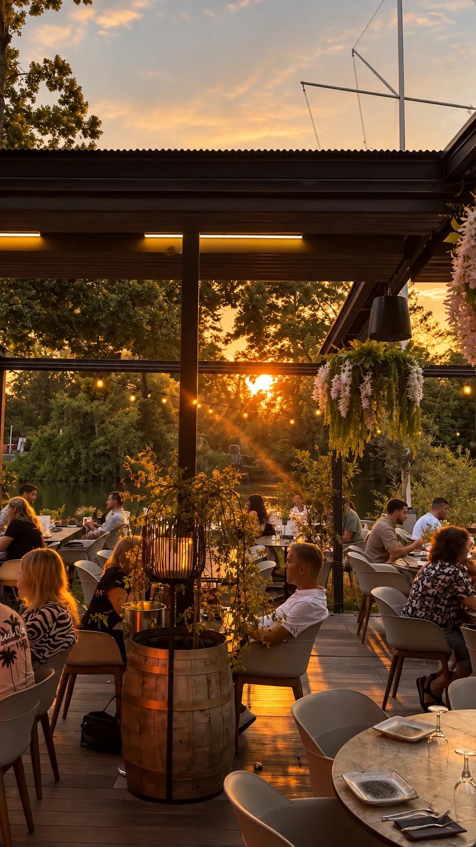 Die Terrasse des Âu Lac bei Sonnenuntergang: Gäste an den Tischen unter der Pergola mit Lichterketten und Blütenampeln, dahinter Bäume und der Fluss